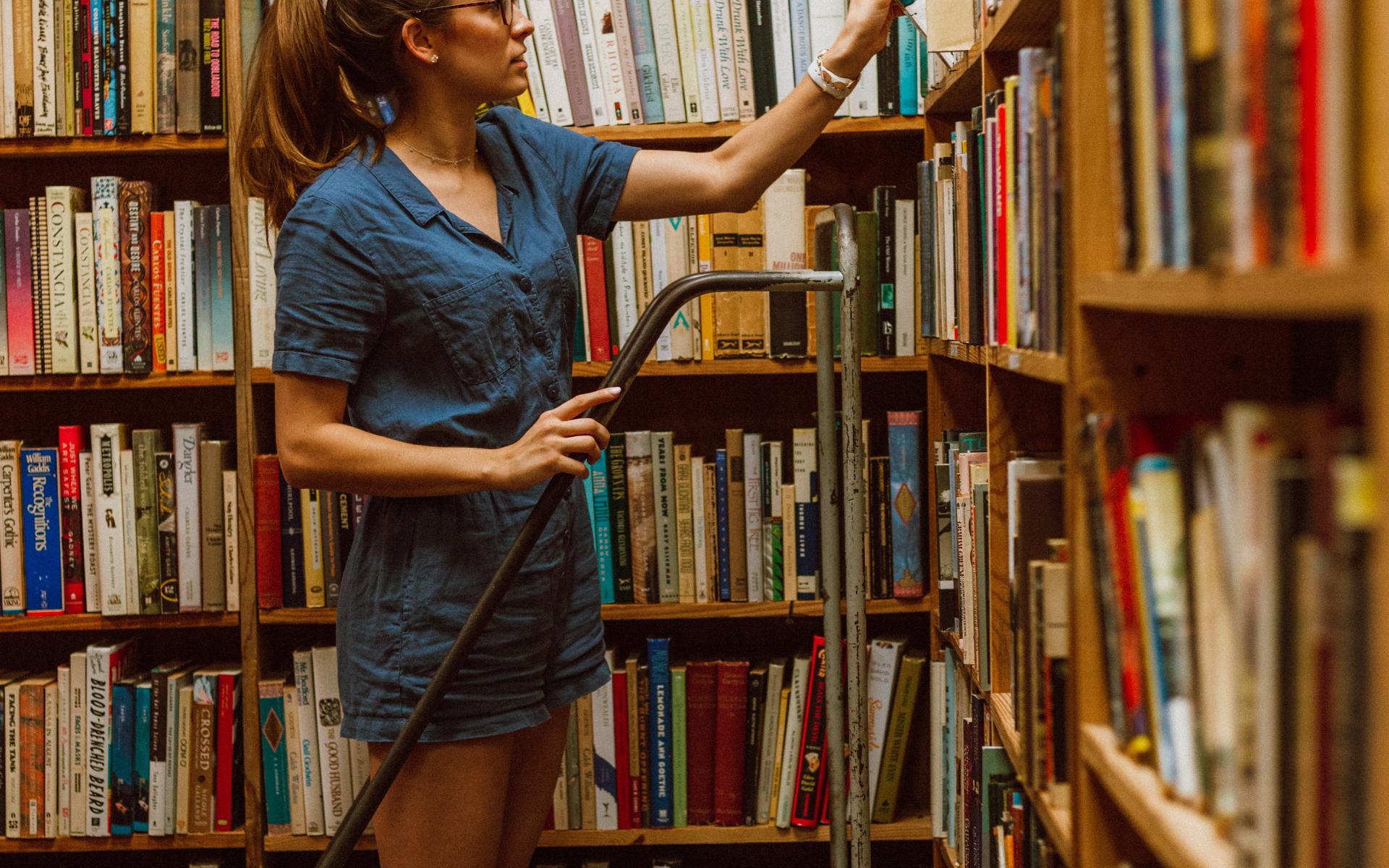 Junge Frau auf einer Leiter vor dem Bücherregal